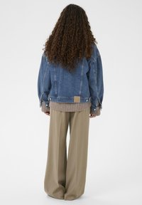 Traper jakna s opuštenim krojem, plave boje, s rebrastim bež manžetama, u kombinaciji s bež hlačama širokog kroja. Sadrži logotip na leđima.