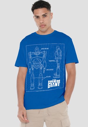 Young man wearing blue T-shirt with white blueprint design of a robot labeled "The Iron Giant" showing front and side views.