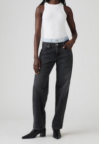 Svart vida jeans med ljusblå midjeband, med hög midja och klassisk femfickdesign. Bärs med en vit linne och svarta klackar.