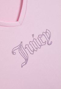 Απαλό ροζ ύφασμα με λαιμόκοψη και τη λέξη «Juicy» γραμμένη με μικρές, λαμπερές στρας σε διακοσμητική γραφή.