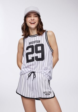Completo in stile basket bianco con righe nere. Presenta la scritta "HOUSTON" e il numero "29" stampati, pantaloni abbreviati abbinati con cordino e logo "MALIBU". Cappello argentato.