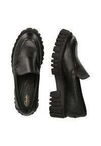 Mocasines de cuero negro con una suela de goma gruesa, que presentan un acabado suave, punta redondeada y sutiles acentos de costura.