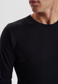 Sort langærmet t-shirt med rund halsudskæring. Fremstillet af ribbet bomuld, med tætsiddende ærmer og en glat overflade.