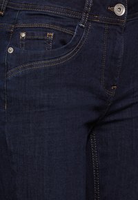Jeans de mezclilla azul oscuro con un diseño clásico de cinco bolsillos, que presentan costuras de cobre y un cierre de botón metálico. Textura suave.