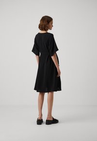 Rochie neagră cu o croială lejeră, mâneci scurte și talie strânsă. O țesătură netedă și fustă până la genunchi. Purtați cu pantofi cu platformă negri.