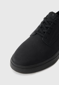 Zapatos negros con cordones, hechos de un material suave, que presentan una puntera redondeada, acentos texturizados y una suela plana de goma.