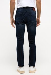 Jeans din denim de culoare albastru închis, cu o croială slim, design cu cinci buzunare și eticheta de piele pe talie. Include accente discrete de broderie.