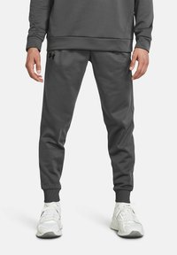 Pantalones deportivos grises con un corte ajustado, puños elásticos y bolsillos laterales, hechos de una tela suave. Presenta un pequeño logo negro en la cadera.