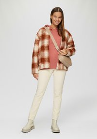 Koszulka w kratę w kolorze rdzy i kremowym, różowa bluza z kapturem, kremowe dopasowane spodnie oraz beżowe botki za kostkę. Zawiera torebkę na ramię.