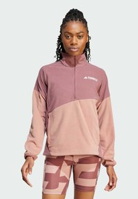 Fleece-pullover vaaleanpunaisissa sävyissä, jossa on puoli-vetoketjukaulus ja TERREX-logo. Yhdistetty kuviollisiin shortseihin, jotka ovat yhteensopivissa väreissä.