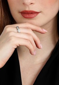 Silverring bärs på en hand med neutral nagellack. Ringen har en slät band med en strukturerad detalj och en polerad yta.