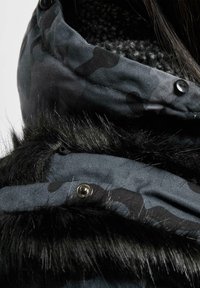 Sort camoufleret jakke med en struktureret sort faux fur krave og knappedetaljer, med en blød grå fleeceforing synlig indeni.