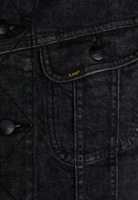 Black denim jacket featuring button closures, chest pockets, and a yellow "Lee" label. The texture is smooth with subtle stitching details.
