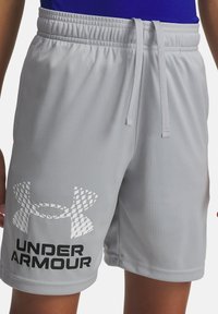 Gaiši pelēki sporta šorti ar elastīgu jostu un auklu, ar lielu Under Armour logotipu uz kreisās kājas, valkāti personā.