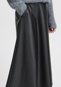 Schwarzer Leder-Midirock mit einer glatten, glänzenden Textur, die elegant von der Taille fällt, kombiniert mit einem grauen Strickpullover oben.