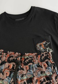 Schwarzes Baumwoll-T-Shirt mit einer Brusttasche und einem gestickten Drachenmotiv. Kombiniert mit gemusterten Shorts in lebhaften Farben und einem elastischen Bund.