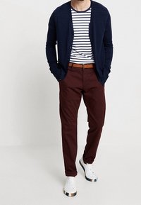 Mörkblå cardigan över en vit och mörkblå randig t-shirt, vinröda byxor, brun bälte och vita sneakers med färgade accenter.