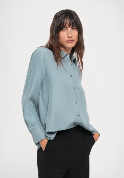 Light blue, long-sleeve button-up shirt with a collar, one chest pocket, and a relaxed fit. Material appears soft with smooth texture.