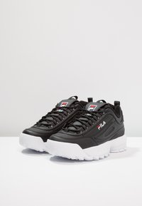 Schwarze Fila Sneaker mit einem glatten Lederoberteil und einer weißen Gummisohle. Zu den Merkmalen gehören dicke Schnürsenkel und ein gepolsterter Kragen für zusätzliche Unterstützung.