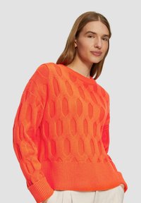Helle orange Strickjacke mit einem Wabenmuster, Rundhalsausschnitt und gerippten Bündchen und Saum. Weiche Textur und lockere Passform.
