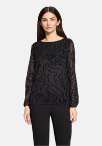 Przezroczysta czarna bluzka z abstrakcyjną fakturą, długimi rękawami, okrągłym dekoltem i subtelnymi detalami, zestawiona z czarnymi spodniami.