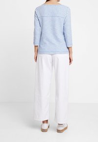 Haut à manches longues bleu et blanc à rayures avec un col rond, associé à un pantalon large blanc et des sabots de couleur claire. Design simple.