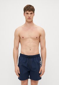 Marineblaue Badeshorts mit elastischem Bund, Kordelzug und seitlichem Grafikdetail. Hergestellt aus glattem, leichtem Stoff.
