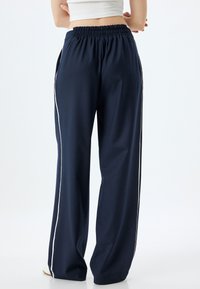 Navyblaue weit geschnittene Hosen aus glattem Stoff mit einem gerafften elastischen Bund und weißen Seitestreifen. Schlichtes, funktionales Design.