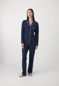 Conjunto de pijama azul-marinho com blusa de manga longa com botão, acabamento em branco e um bolso, acompanhado de calças retas combinando.