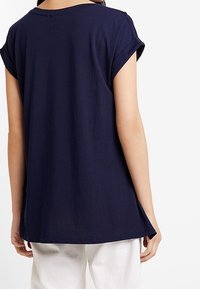 Námořnická modrá tričko s ohrnutými krátkými rukávy, volný střih a zaoblený lem. Měkký materiál, jednoduchý design bez ozdob.