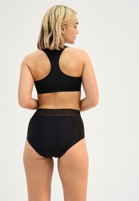 Top sportivo nero con scollatura alta e design racerback, abbinato a slip neri a vita alta con un cinturino testurizzato.
