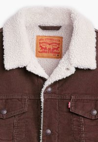Bruine ribfluwelen jas met witte sherpa kraag, zilveren drukknoopsluiting, twee borstzakken en een rode Levi Strauss-label aan de binnenkant. Maat M.