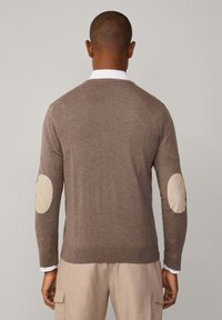 Maglione lavorato a maglia marrone con una vestibilità classica, maniche lunghe e contrasti di materiali color crema sui gomiti. Tessuto morbido e dettagli a coste sull'orlo.