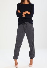 Laivastonsininen neulospaita pitkällä hihalla, yhdistettynä harmaisiin jogger-housuihin, joissa sivuraitoja ja kiristysnauha. Asustettu vaaleanpunaisilla korkeakoroisilla kengillä.