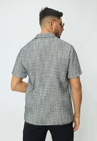 Chemise à manches courtes en motif géométrique noir et blanc, faite d'un tissu lisse. Dotée d'un col classique et d'une coupe décontractée.