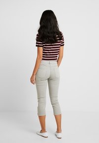 Pantaloni capri grigio chiaro, design a vita media, cinque tasche, forma aderente, abbinati a una maglietta a maniche corte a righe bordeaux e bianche.