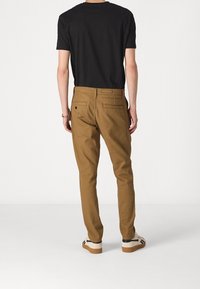 Bruna bomullsbukser med smal passform, med två bakfickor, subtil sömnad och en svart T-shirt med kort ärm.