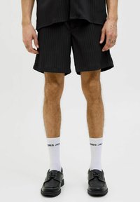 Sorte ribbede shorts lavet af stof, med lige snit og en ren kant. Kombinationen med hvide sokker og sorte snørebåndssko.
