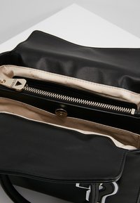 Zwarte leren handtas met een crèmekleurige voering, voorzien van een gouden ritssluiting, een binnenvak met rits en merkopdruk op de voering.