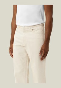Pantalones de algodón beige con corte recto, que cuentan con bolsillos delanteros y cierre de botón. Textura suave, diseño minimalista.