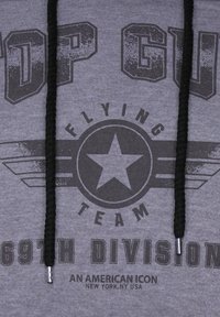 Grå hoodie med texten "TOP GUN" och "FLYING TEAM". Har en stjärngrafik, svarta dragsnören och silverfärgade metallaccenter.
