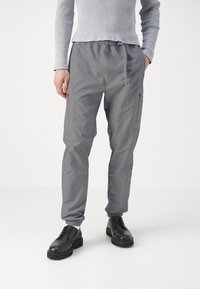 Grå cargobyxor med elastisk midja, sidofickor med dragkedja och fållade nederkanter, i kombination med svarta snörskor.