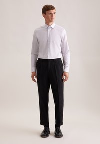 Camicia a righe bianche e grigie chiare con bottoni sul davanti, indossata con pantaloni scuri su misura e scarpe nere. Il tessuto appare liscio e aderente.