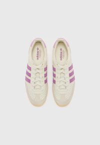 Adidas sneakers i krämfärg med ljuslila accenter. Har slät läder, perforerad tå och tre lila ränder. Gummi yttersula.