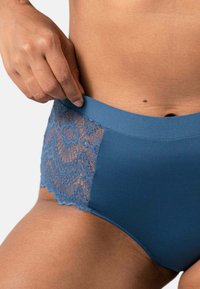 Höga blå trosor med en blommig spetspanel på ena sidan och ett slätt, stretchigt tyg för komfort.