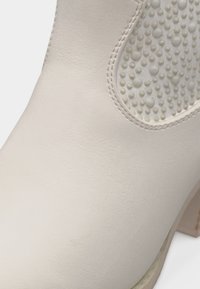 Κοντινό πλάνο ενός λευκού δερμάτινου μποτάκι με υφασμάτινη ελαστική οβάλ επιφάνεια και λεπτομερείς ραφές κοντά στην περιοχή του αστραγάλου.