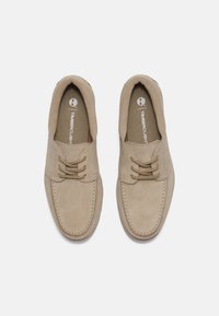 Scarpe in suede beige con lacci, punta arrotondata e cuciture visibili attorno alla suola. Presentano un interno imbottito per il massimo comfort.
