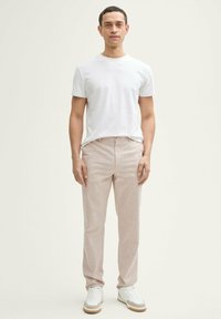 Pantalones de lino beige claro de corte recto, combinados con una camiseta de algodón blanca lisa y zapatillas blancas con acentos beige.