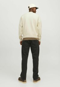 Pull en crème clair avec un ourlet côtelé, porté par-dessus une chemise marron, associé à un jean noir et des chaussures marron foncé, complété par une casquette claire.