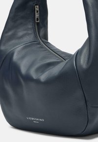 Granatowa skórzana torebka o miękkiej, gładkiej fakturze, z zamknięciem na zamek, zaokrąglonym kształcie i dyskretnym logo na spodzie.